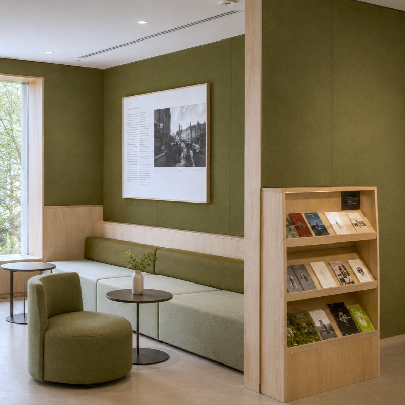 Moderner Loungebereich mit Sofa, Sessel, kleinen Tischen und einem Bücherregal in einer Galerie- oder Hotellobby.