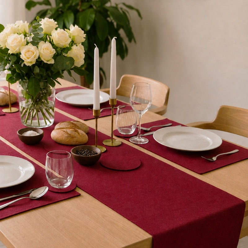 Festlich gedeckter Esstisch mit rotem Tischläufer, weißen Rosen, Kerzen, Brot und Geschirr.