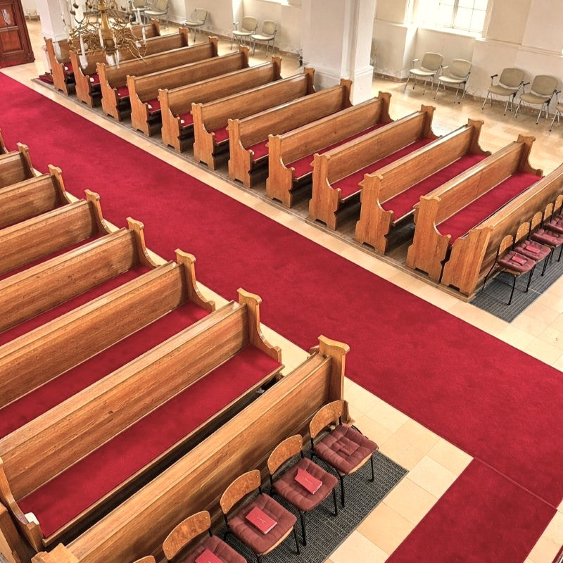 Innenraum einer Kirche mit Holz-Kirchenbänken und Stühlen, die kardinalrote Filzauflagen haben.
