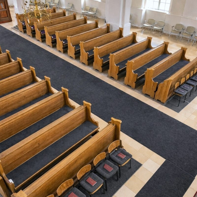 Innenraum einer Kirche mit Holz-Kirchenbänken und Stühlen, die anthrazitfarbene Filzauflagen haben.